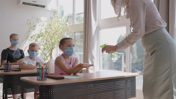 The Teacher Treats the Hands of an Antiseptic Girl in the Classroom at School Before Class