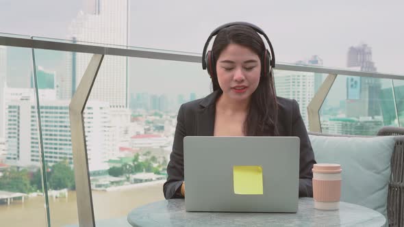 Happy asian woman wear headset communicating by conference call speak looking at computer at cafe