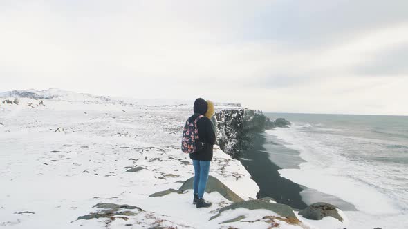 Young Woman Tourist Walks at the Top of the Cliff Around Reynisfjara Beach and Dyrholaey Lighthouse