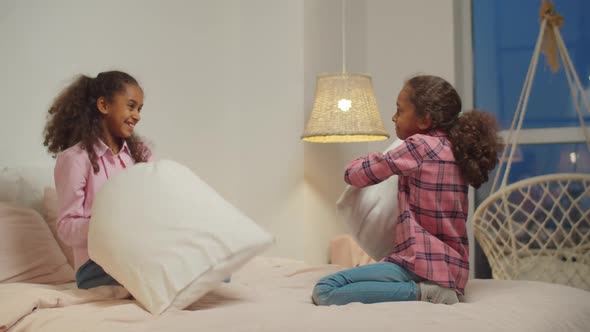 Black Preadolescent Sisters Pillow Fighting on Bed alt
