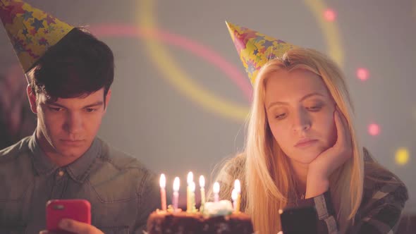 The Sad Girl and a Man in Birthday Hats Sitting in Front of Cake with Candles