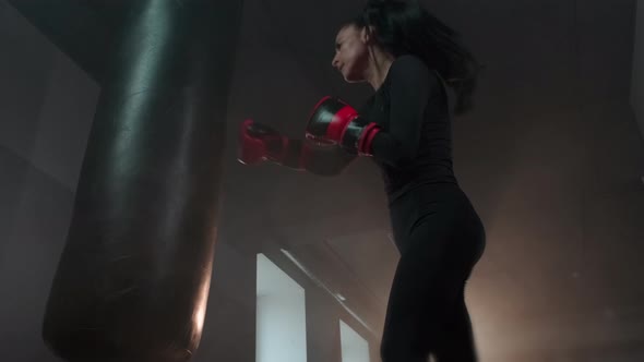 Fighter girl punches in boxing gloves and kicks a punching bag.