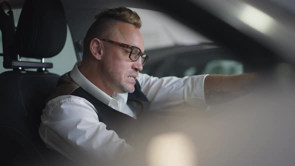Tattooed Adult Caucasian Man in Eyeglasses with Mohawk Haircut Sitting on Driver's Seat in Car
