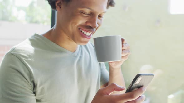 African american man using smartphone and drinking coffee at home