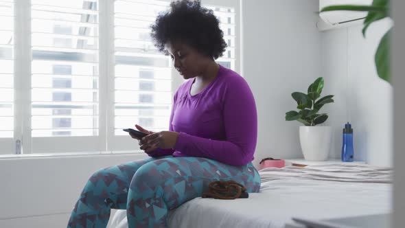 African american female plus size sitting on bed using smartphone