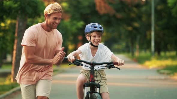 A happy father is teaching his son to ride a bicycle while helping him