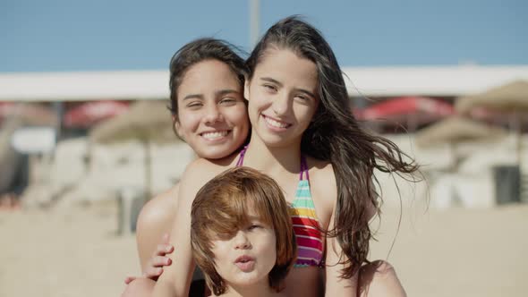 Front View of Happy Kids Sitting Together on Beach and Hugging