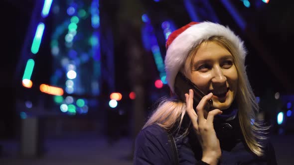 a woman chatting on her smartphone wearing a Santa hat is a night city.