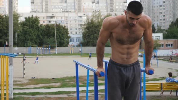 Strong Sporty Man Doing Push Ups on Parallel Bars at Sports Ground
