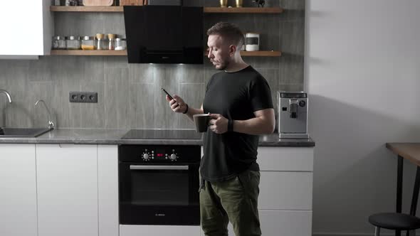 Young Man in His Kitchen with a Smartphone in His Hand