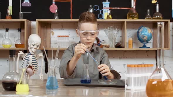 Laboratory Experience in a Chemistry Lesson Boy in Protective Glasses Pours a Blue Liquid Into a
