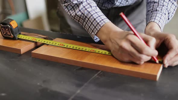 Male Hands Using a Yellow Tape Measure To Measure a Piece of Wood