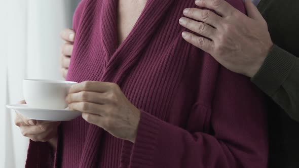 Husband gently hugging his wife by shoulders, cozy home atmosphere, love story