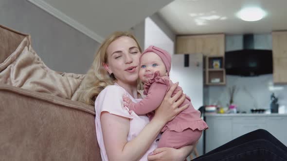 Mother and Baby Girl with Blond Hair and Blue Eyes in Pink Clothes Huddle Together Against the