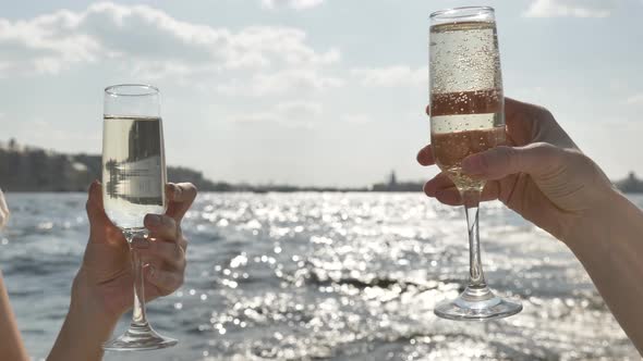 Ladies Hands Hold Glasses with Champagne Against River