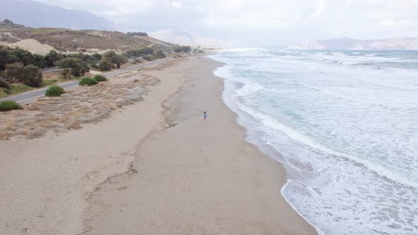 Drone footage of a woman running along the ocean coastline and leaving footprints in the sand.