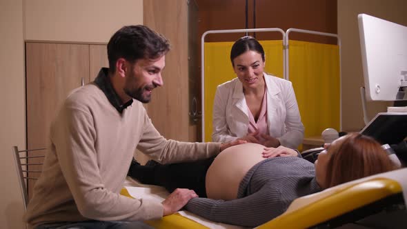 Happy Man Stroking Pregnant Wife's Belly in Clinic
