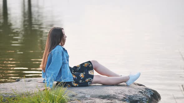 A Girl Sits By the Lake on a Rock