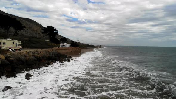 Aerial drone shot on a cloudy day low over the Pacific Ocean waves curling and crashing against the