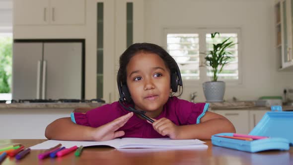 Hispanic girl sitting at table having video call wearing headset