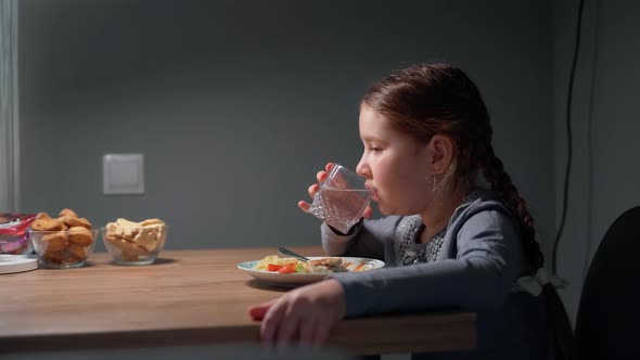 The child eats pasta with a fresh salad of tomato, pepper and round cheese and drink water