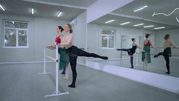 Side View Three Ballerinas Rehearsing Raising Leg Bending Forward Reflecting in Mirror in Dance