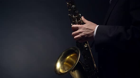 Close-up view of the profile of musician in suit playing a gold saxophone on dark studio background