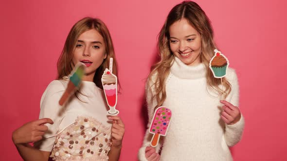 Two beautiful carefree women make funny faces. Positive models posing over pink background