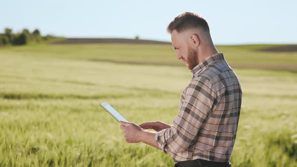 The Farmer is Standing Near the Field and Working with a Tablet