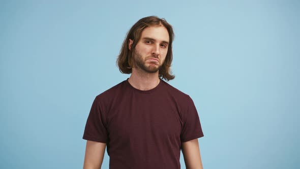 Young Bearded Guy is Shaking His Head Showing Thumbs Up Winking and Smiling While Posing on Blue