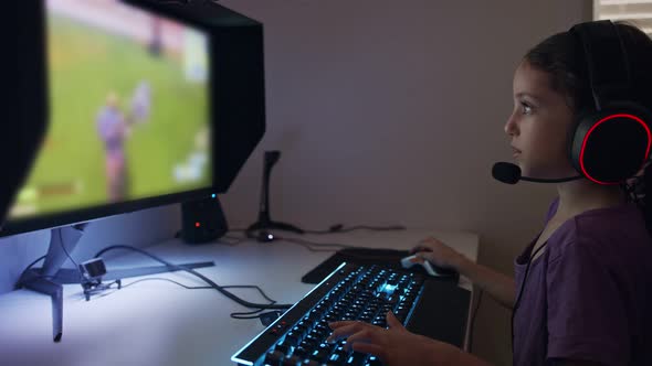 Young girl sitting in front of a computer, playing a game wearing a headset