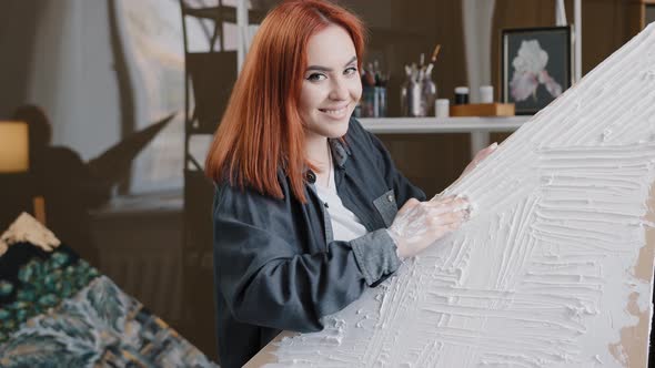 Redhaired 20s Caucasian Woman Female Artist Girl Painter in Workshop Draws Puts Plaster on Canvas