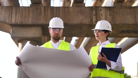 Two Civil Engineers a Young Man and a Young Woman Working on a Project Wearing Safety Helmets are