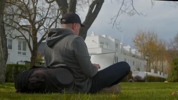 Young Man is Sitting in a Park in a Tourist Place Working on a Laptop