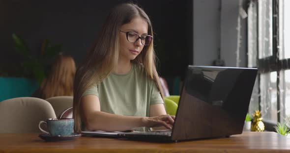 Young Woman Sitting at the Table in a Cafe and Working Online on Her Laptop