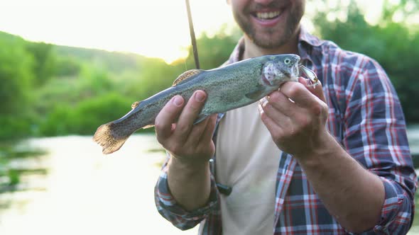 Fisherman Rests on the River and Catches Trout Smiles and Shows the Fish in the Camera