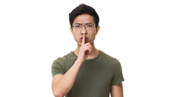 Portrait of Brunette Chinese Man Wearing Glasses and Basic Tshirt Doing Shh Gesture with Index