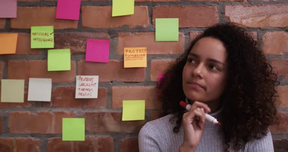 Thoughtful creative businesswoman writing on sticky notes in modern office