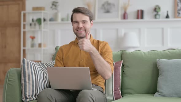 Young Man Showing Thumbs Up Sign While using Laptop in Office