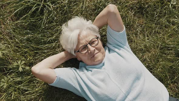 Senior Woman, Pensioner Lying on the Grass with Hands Under Her Head in the Garden Overhead Close Up