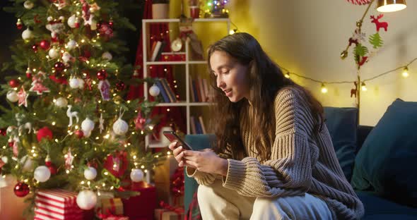 Young Woman Chatting in Smartphone Sitting on Sofa in Living Room