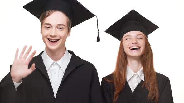 Ginger Caucasian Graduate Girl in Black Robe and Square Academical Cap Laughing on White Background