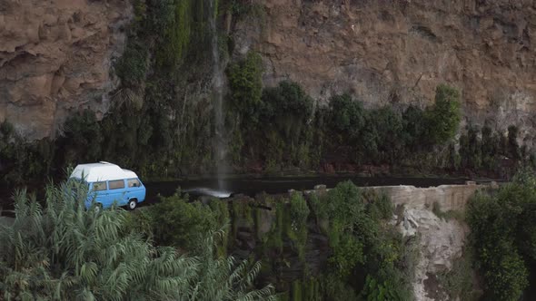 Aerial shows a VW-Camper van driving through a waterfall, Cascada dos Anjos, Ponta do Sol, Madeira