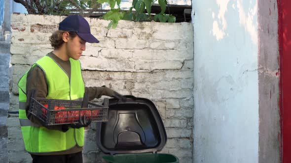 Food Waste at Retail. A supermarket worker throws spoiled rotten unsold vegetables into a dumpster