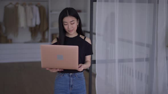 Live Camera Follows Smiling Confident Gorgeous Asian Young Woman Walking with Laptop in Bedroom