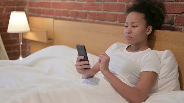 Young African Woman Using Smartphone in Bed