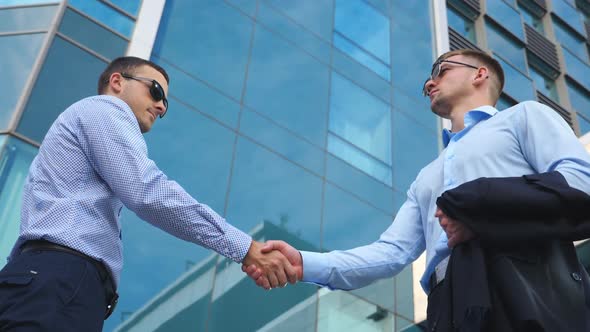 Two Young Male Colleagues Shaking Hands Near Office Building. Handsome Businessmen Greeting Each