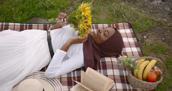 Black Woman with Flowers Laying on Picnic Blanket
