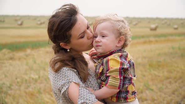 Young Woman with Fair-haired Little Son in Her Arms in the Middle of a Wheat Field