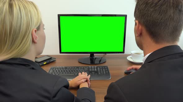 Two Office Workers Sit at A Desk and Talk, the Man Works on A Computer with A Green Screen 